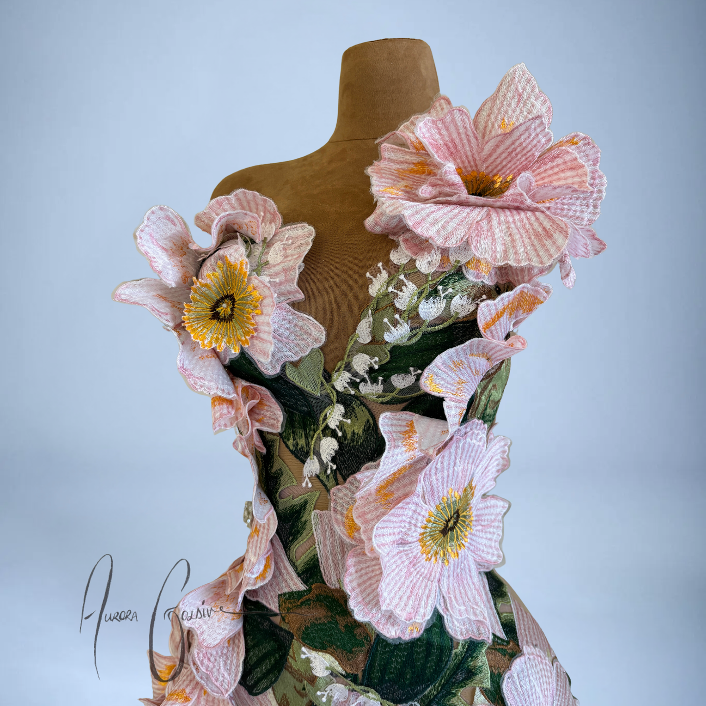 Close-up of pink floral appliqués on Amelia Gown wedding dress on a mannequin against a light blue background